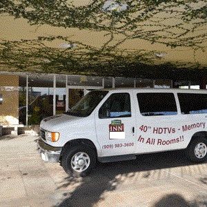 A white van with &ldquo;40&rdquo; HDTVs and &ldquo;Memory Foam Beds&rdquo; printed on the side, parked in front of a building under a tree canopy.