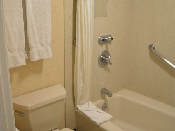 A compact hotel bathroom with a toilet, bathtub, shower curtain, towel rack, and a small mirror on beige tile walls.