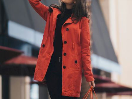 A stylish woman in a red coat carries shopping bags while posing on a city street.